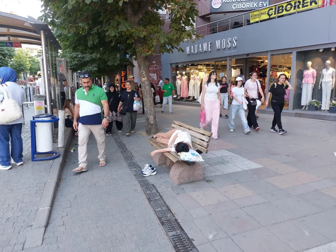 Sıcaktan bunalan genç yastığını alıp bankta uyudu