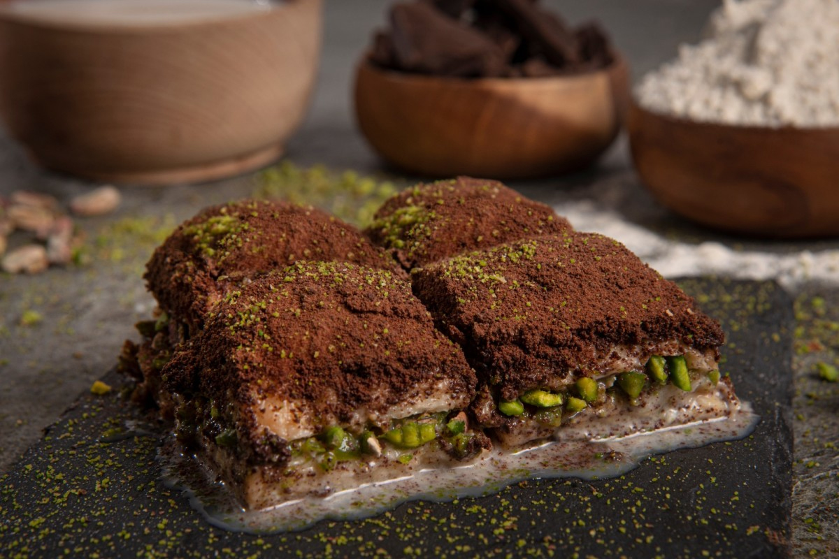 <strong>SÜTLÜ SOĞUK BAKLAVA NASIL YAPILIR?</strong>
İlk olarak şerbetimizi yapmakla başlayın. Tencereye su, süt ve şekeri koyarak şeker eriyinceye kadar karıştırın. 5 dakika kaynadıktan sonra ocaktan alın ve soğumaya bırakın.
Tereyağını eritin. Üzerin de oluşan köpüğü almak içinde süzgecin içine havlu kağıt serin ve tereyağını dökün. İyice süzüldükten sonra köpükten arınan tereyağının içerisine sıvı yağ ekleyin.
Yufkalarınızı tezgaha serin ve borcam boyutunda kesin. Yufkaları ikiye ayırın. Alt tabana 20 yaprak, üst tabana da 22 yaprak kullanın. Üzeri için ayırdığınız yufkaları temiz bir beze sarın ki kurumasın. Çok ince oldukları için çabuk kuruyorlar.
Borcamı yağlayın. Bir yaprak yufkanızı borcama yerleştirip üzerini yağlayın.
Her yufka arasını yağlayarak üst üste dizin.
Geri kalan yufkaları da aynı şekilde her katı yağlayarak üst üste dizin. İstenilen büyüklükte kare kare keserecek üzerine kalan yağı sürün.
170 derecelik önceden ısıtılmış alt üst ayar fırında yaklaşık 45 dakika üzeri güzelce kızarana kadar pişirin. Altının iyice piştiğinden emin olun.
Baklavanızı piştikten sonra 10 dakika dinlendirin. İlk sıcağı çıkan baklavanıza soğuk şerbeti kepçe yardımıyla dökün. 2-3 saat dinlenmeye bırakın.
Tatlının üzerine kakao ve pudra şekerini karıştırın ve her yerine gelecek şekilde eleyin. Rendelenmiş çikolatayı da üzerine serpin.
En son olarak Antep fıstığıyla süsleyip servis edebilirsiniz. Afiyet olsun.