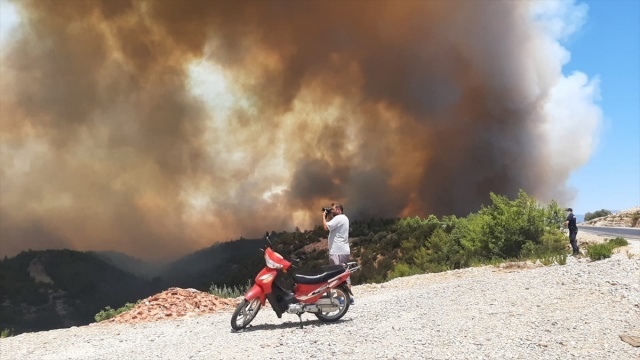 Antalya-Manavgat D-400 karayolu üzerinde araçlar, gökyüzünü kaplayan ve kilometrelerce alanda etkili olan siyah dumanlar gölgesinde ilerliyor.