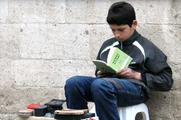 Boyacı çocuk, iş arasında kitap okuyor
