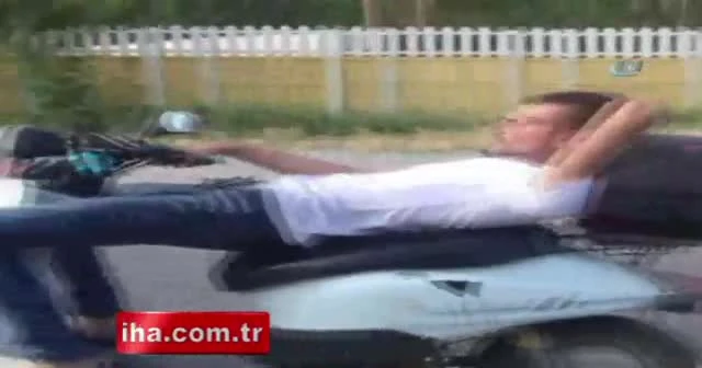Koltuğuna sırt üstü yattığı motosikleti tek elle kullanıyor